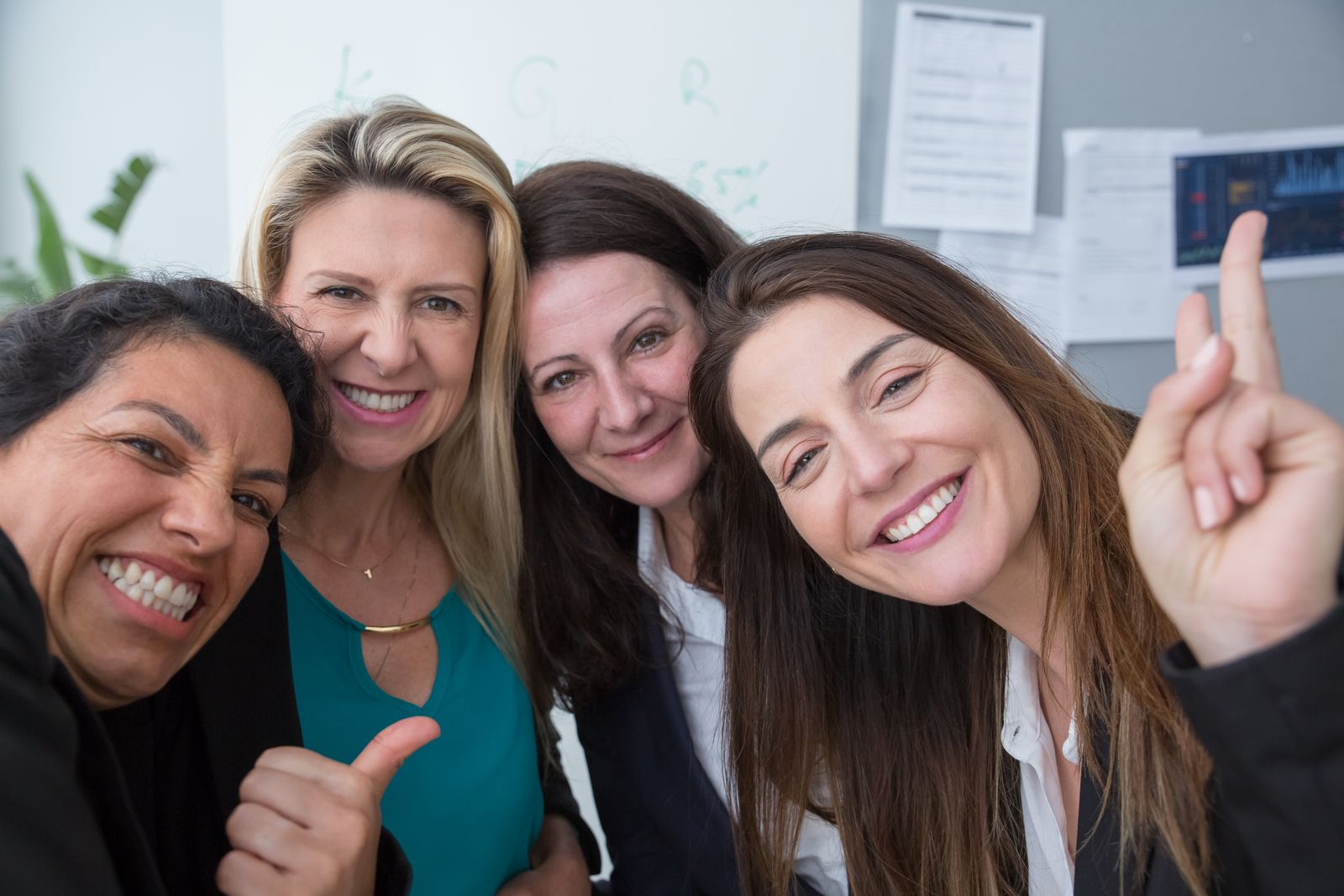 Four female colleagues smiling and posing for a group photo at the office, exuding teamwork and positivity.